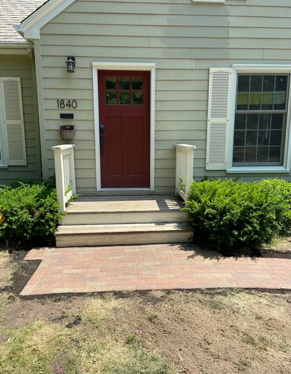 Front entrance of a house featuring a red door, wooden steps, and landscaped greenery.