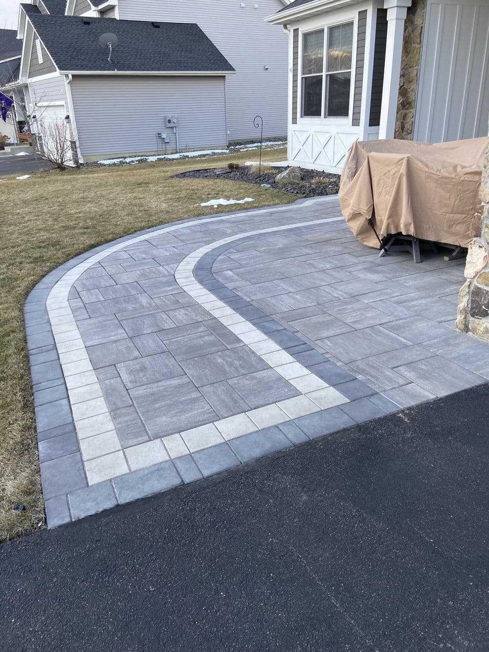 Patterned concrete driveway with gray and white design, featuring lawn and covered furniture.