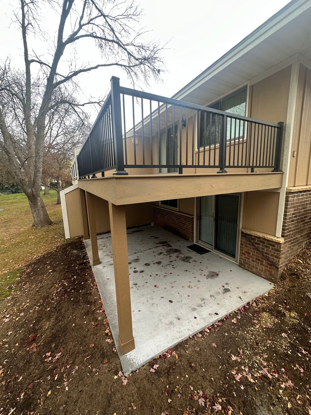 Exterior view of a modern home balcony with black railing and concrete patio below.