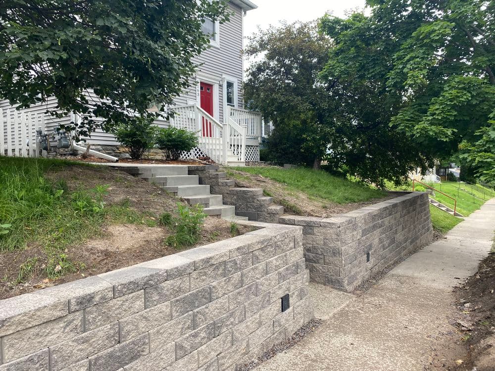 Residential home with red door, stone steps, and landscaped garden by sidewalk.