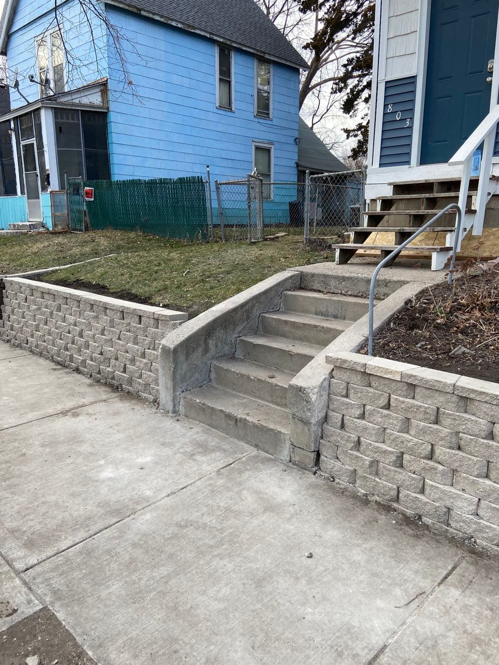 Concrete steps leading to a blue house with a fenced yard and garden area.