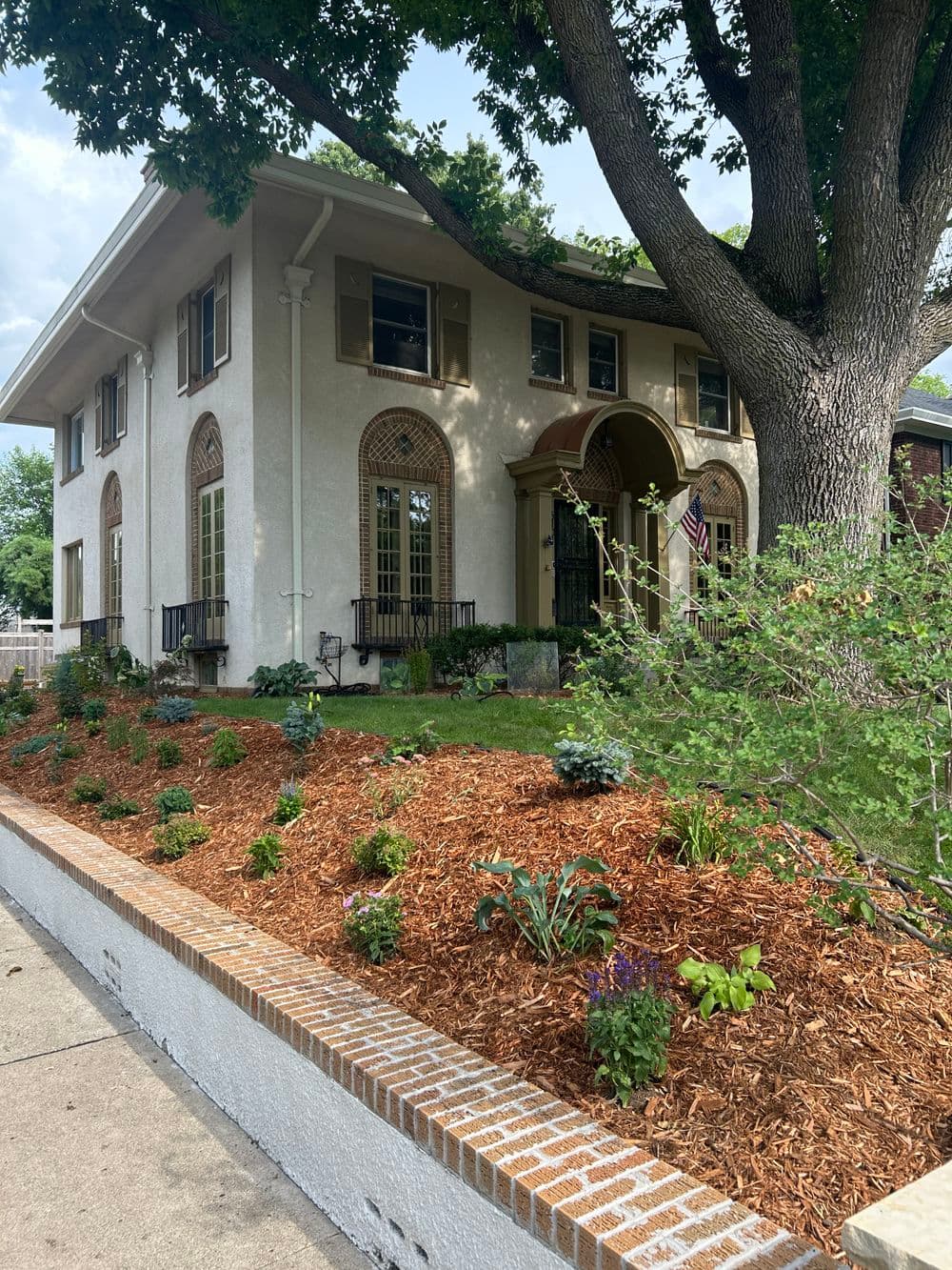 Elegant two-story home with decorative windows, lush garden, and vibrant landscaping.