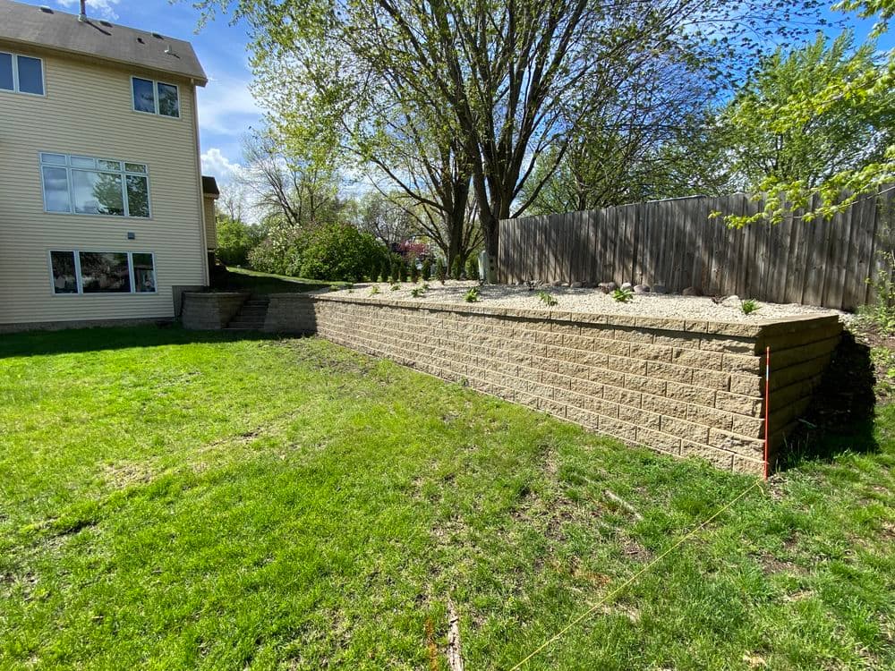 Landscaped backyard with stone retaining wall, grass area, and house in the background.
