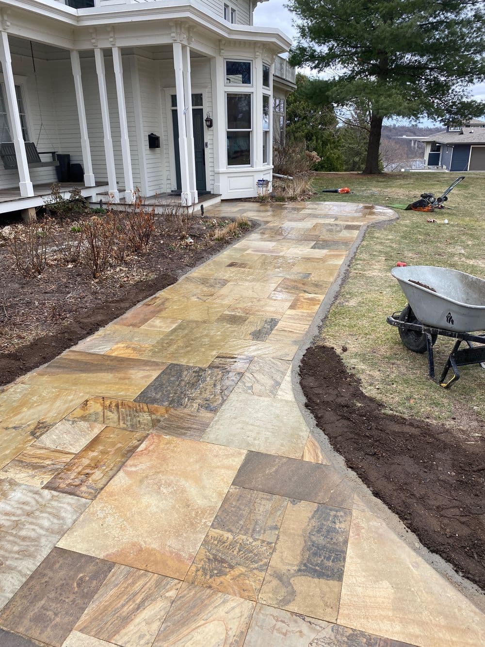 Newly installed stone pathway leading to a house, surrounded by landscaping and tools.