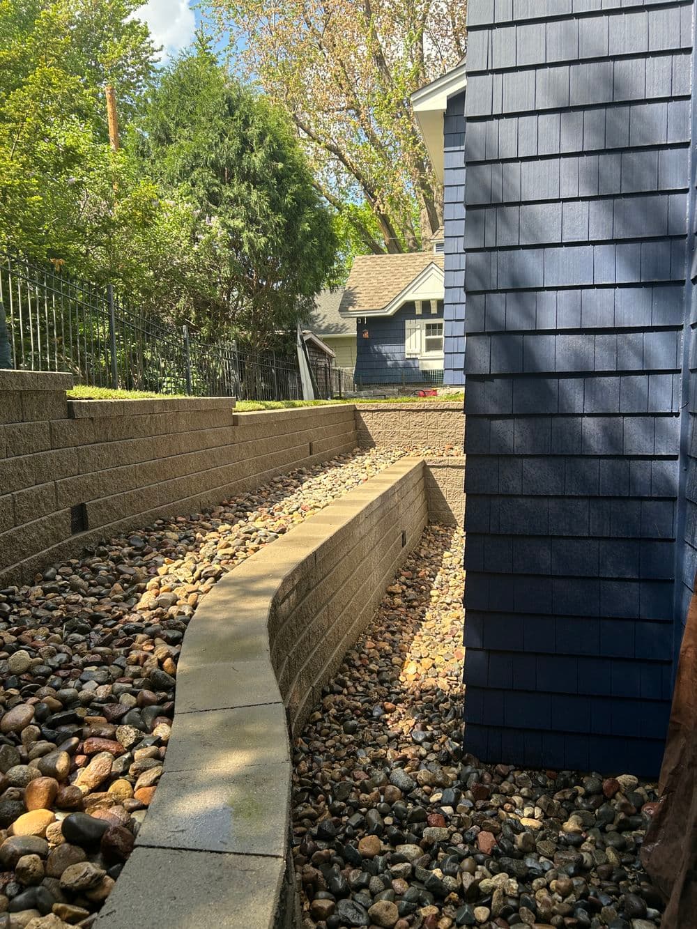 Curved stone pathway with pebbles alongside a blue house and lush greenery.