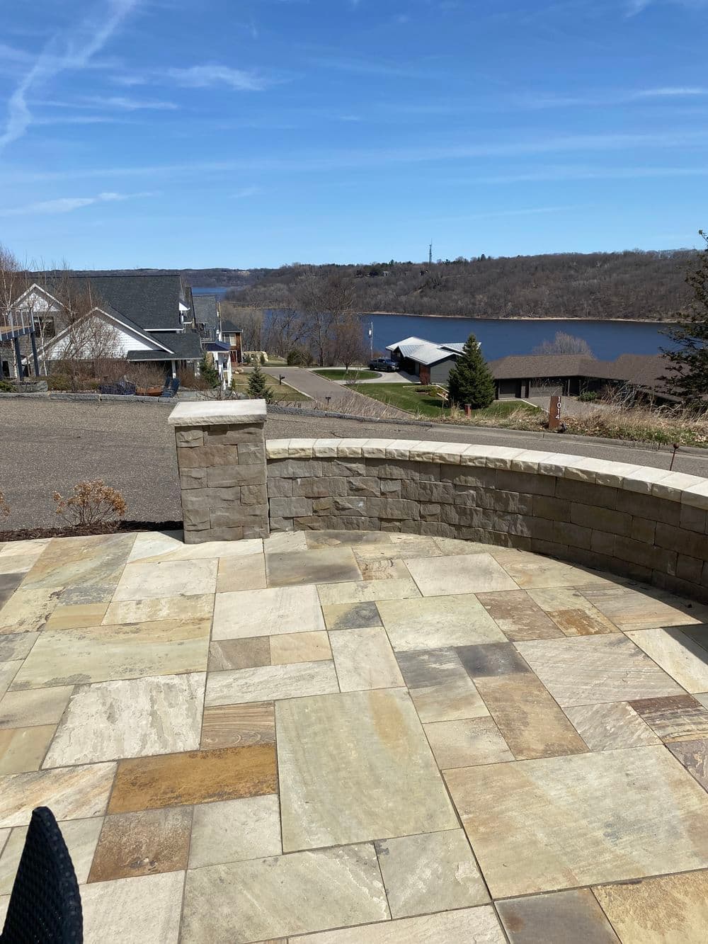 Stone patio overlooking a tranquil river and scenic residential homes. Ideal for outdoor relaxation.