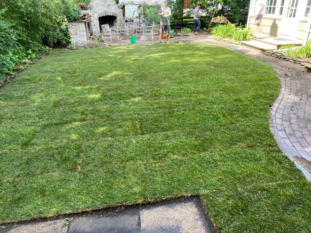 Lawn installation in a backyard with workers, fresh grass, and patio seating area.