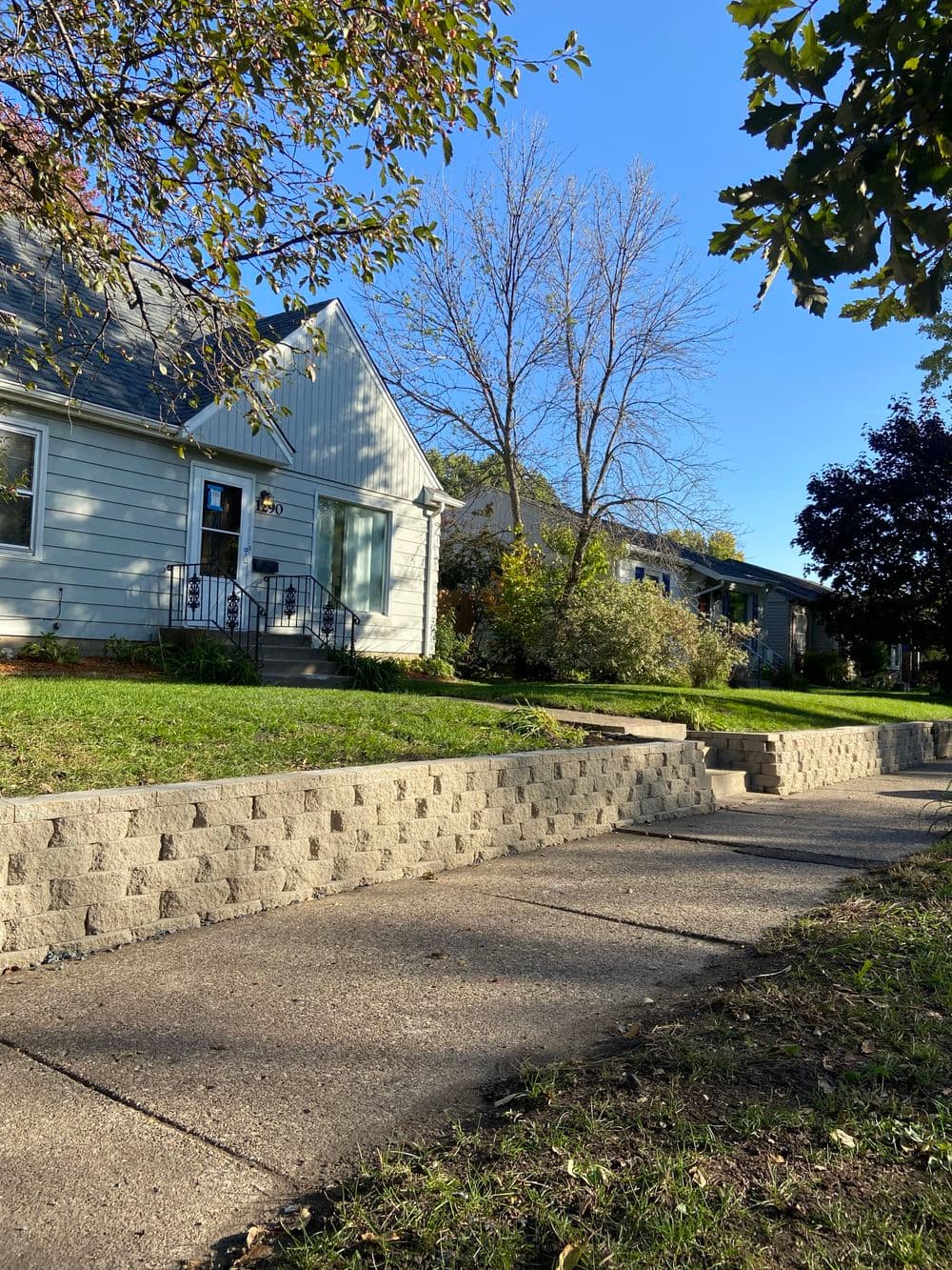 Residential neighborhood with houses, trees, and a paved sidewalk on a sunny day.