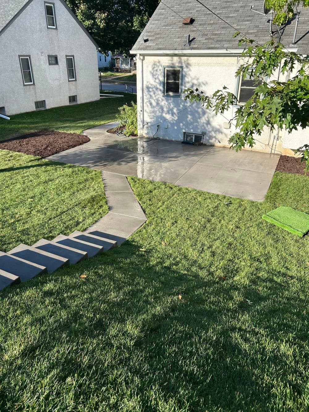 Concrete patio and landscaped yard with stepping stones leading to a house.