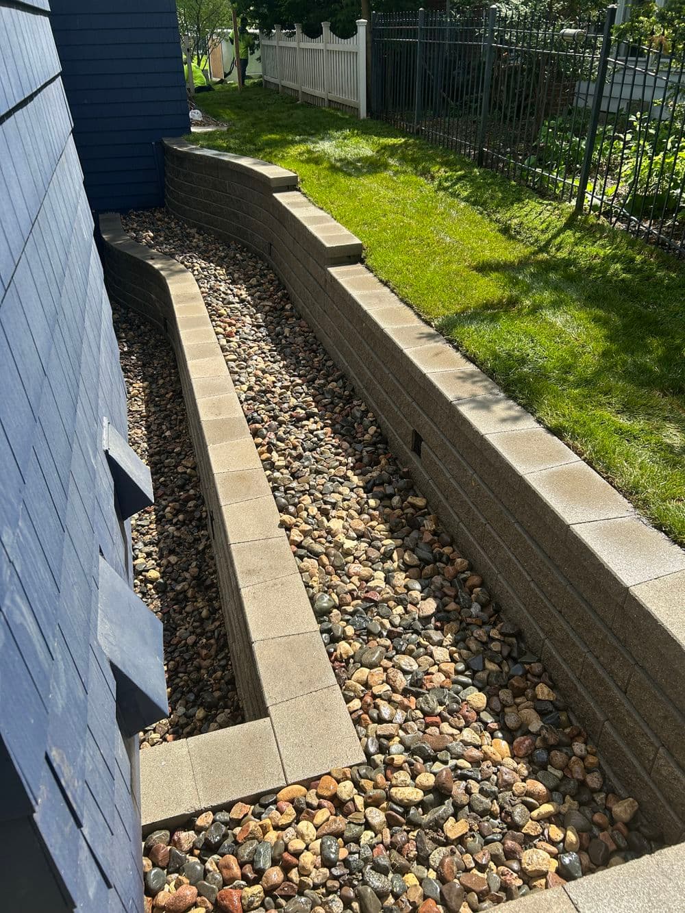 Landscape drainage system featuring stone-lined channels and retaining walls in suburban yard.