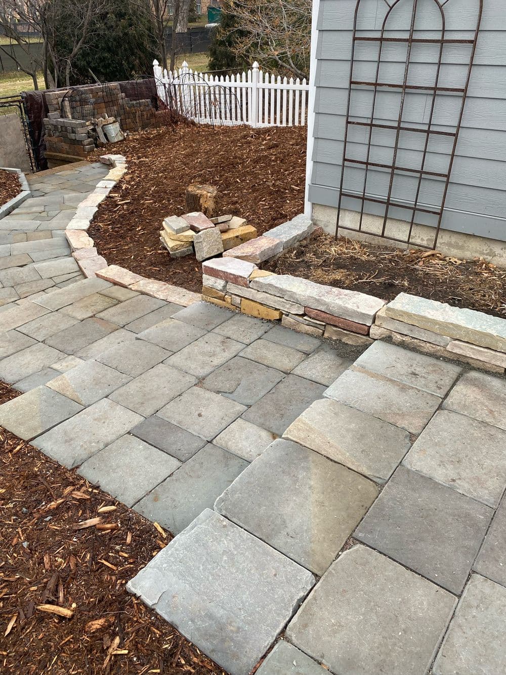 Stone pathway leading to a garden area with mulch, rocks, and a white fence.