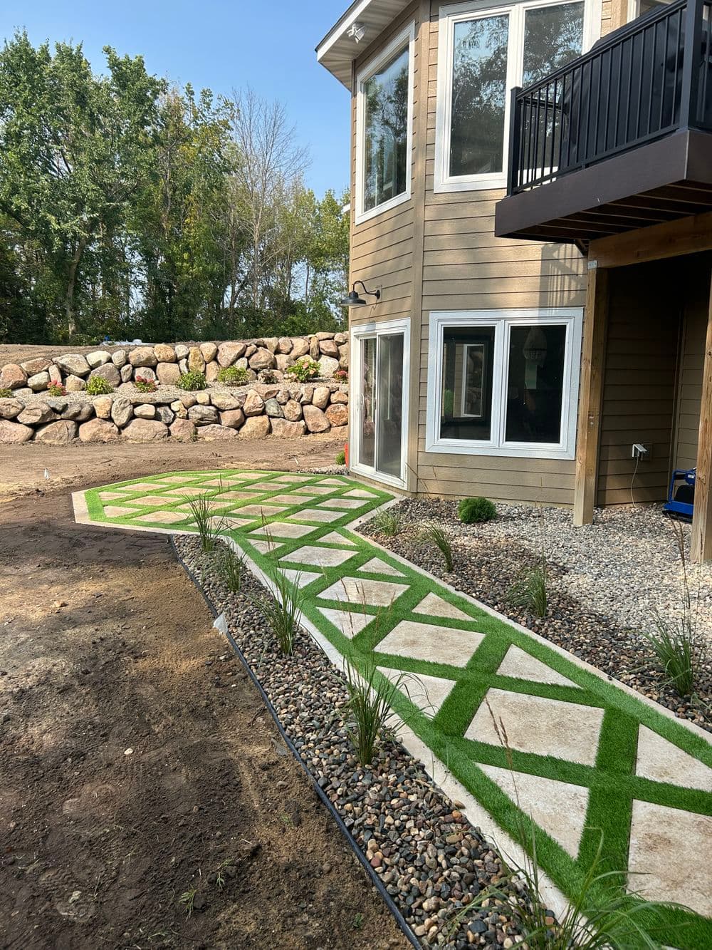 Stylish backyard pathway with green turf and stone accents next to modern home exterior.