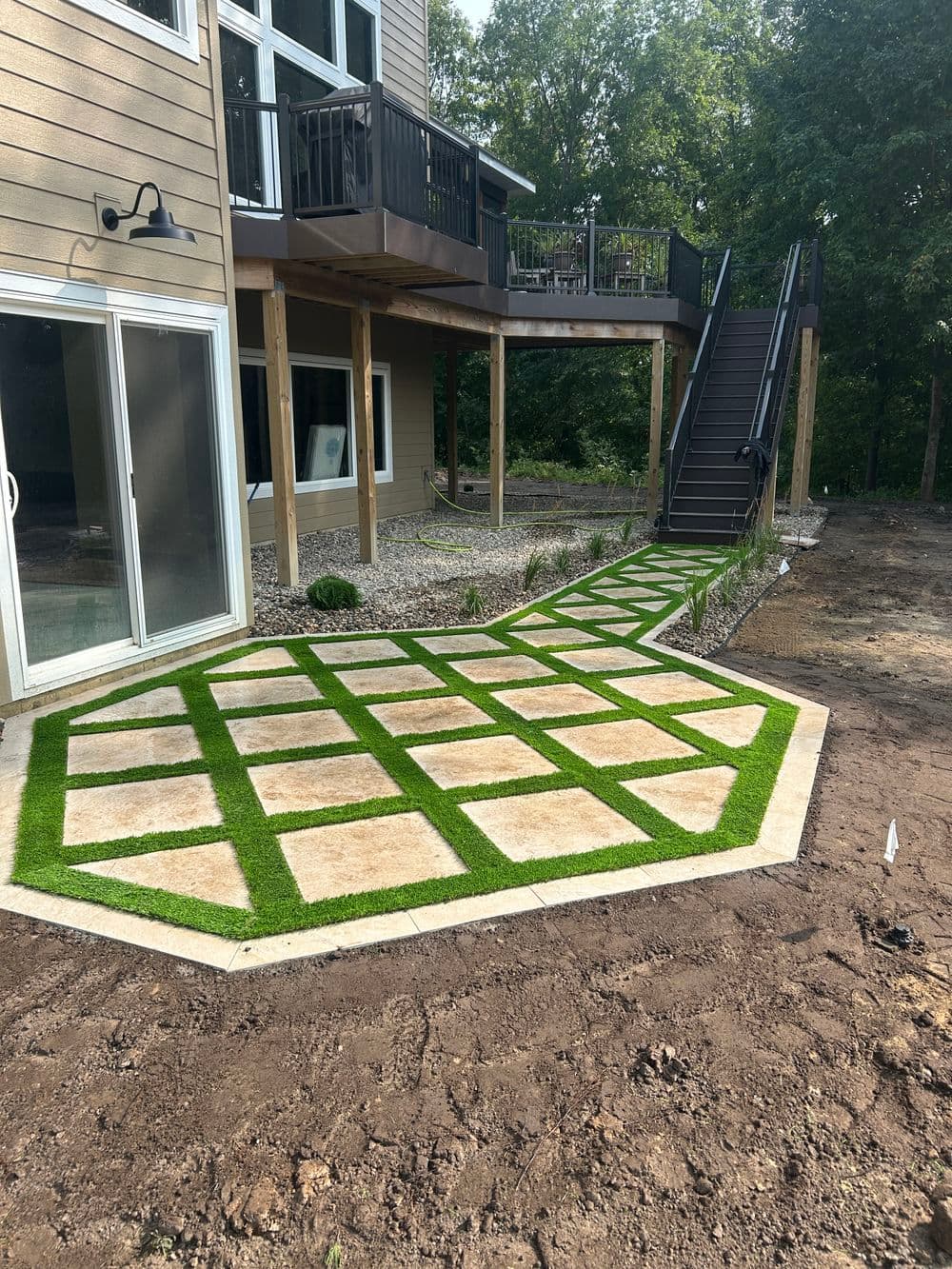Modern backyard pathway with stone tiles and grass, leading to a wooden deck and stairs.