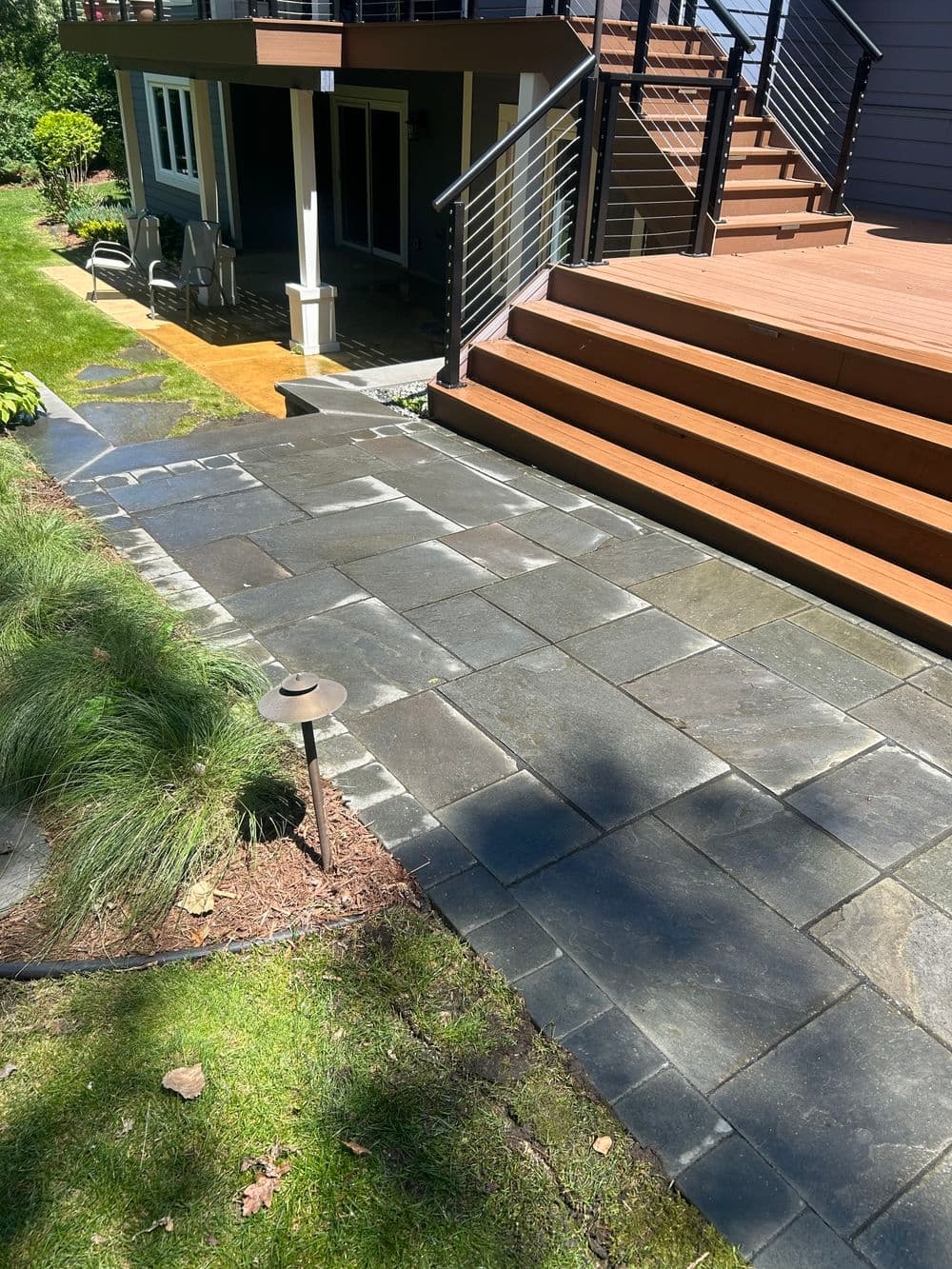Modern stone patio pathway leading to a wooden deck in a landscaped garden.