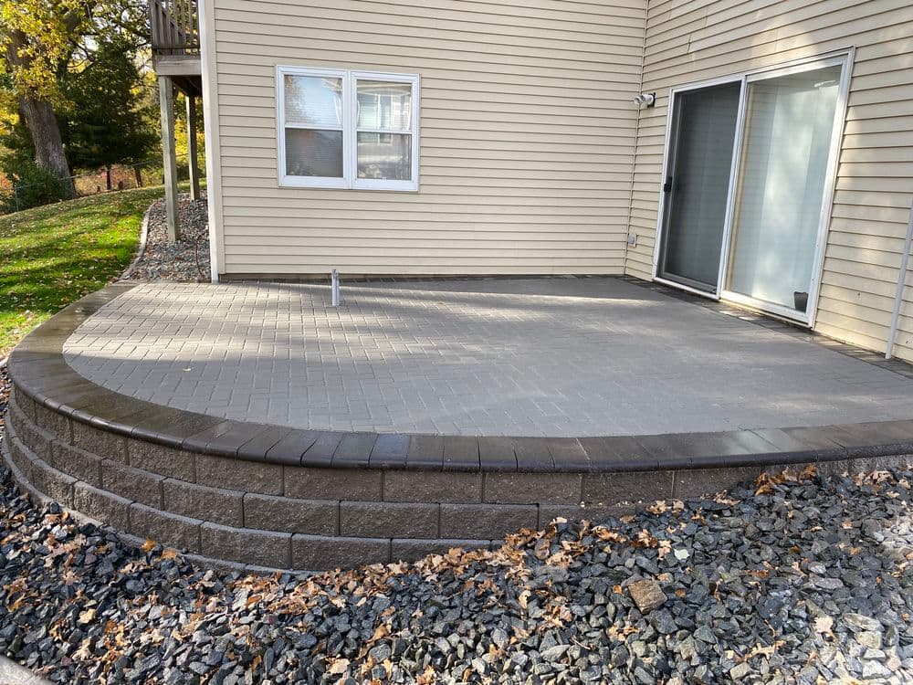 Patio featuring curved stone wall and paved surface, adjacent to home with sliding door.