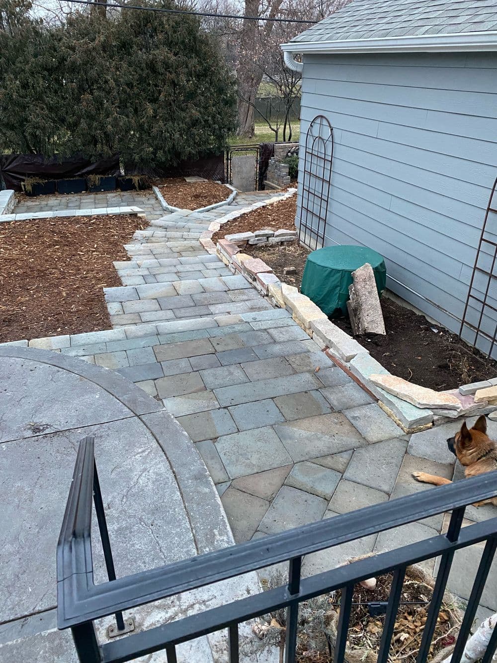 Paved pathway leading to landscaped yard with greenery and a dog. Perfect outdoor design.