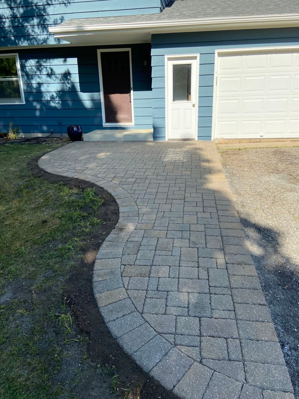 Newly paved curved walkway leading to blue home entrance with garage.
