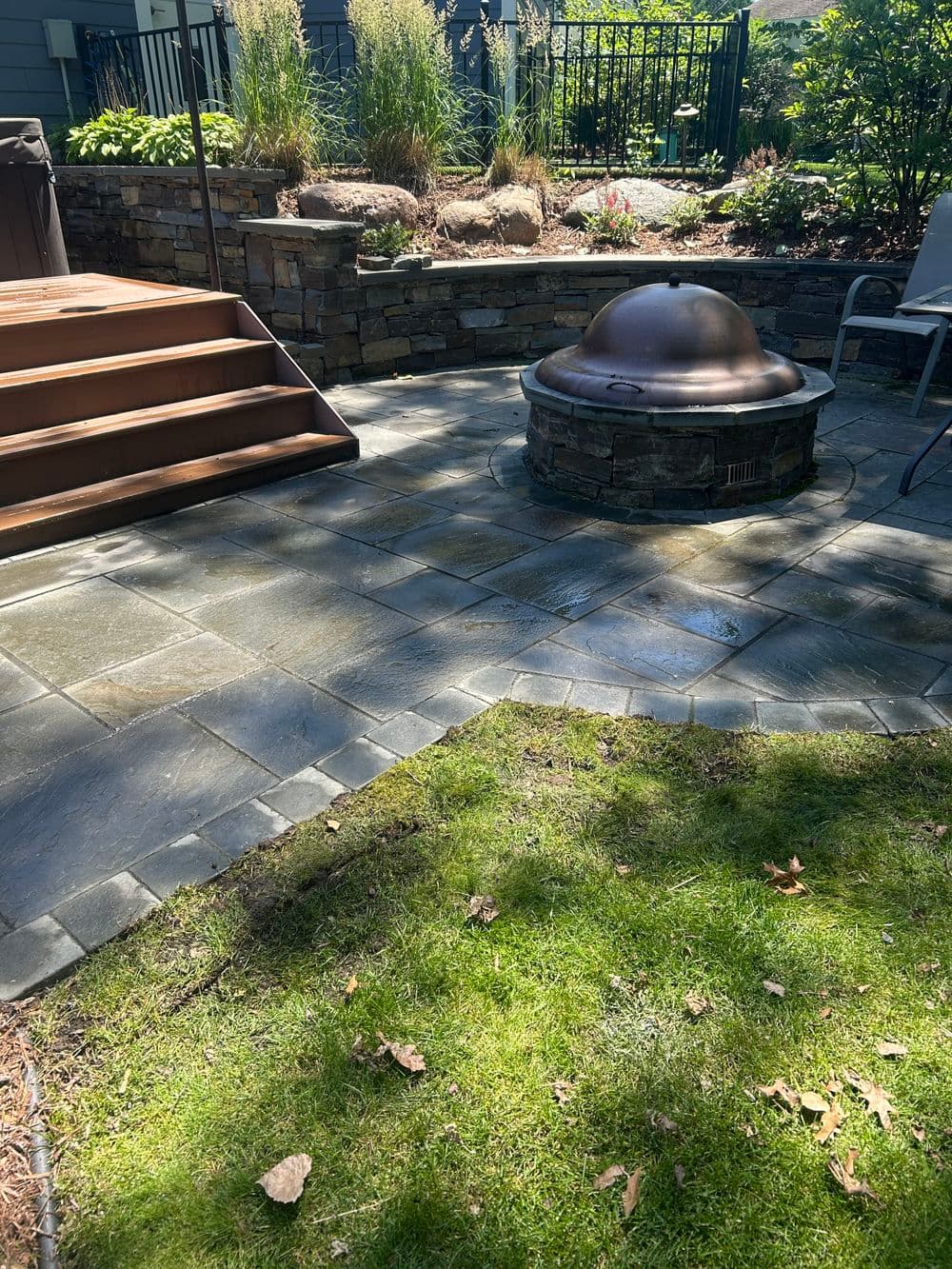 Patio area featuring stone wall, steps, and a bronze fire pit in a landscaped yard.