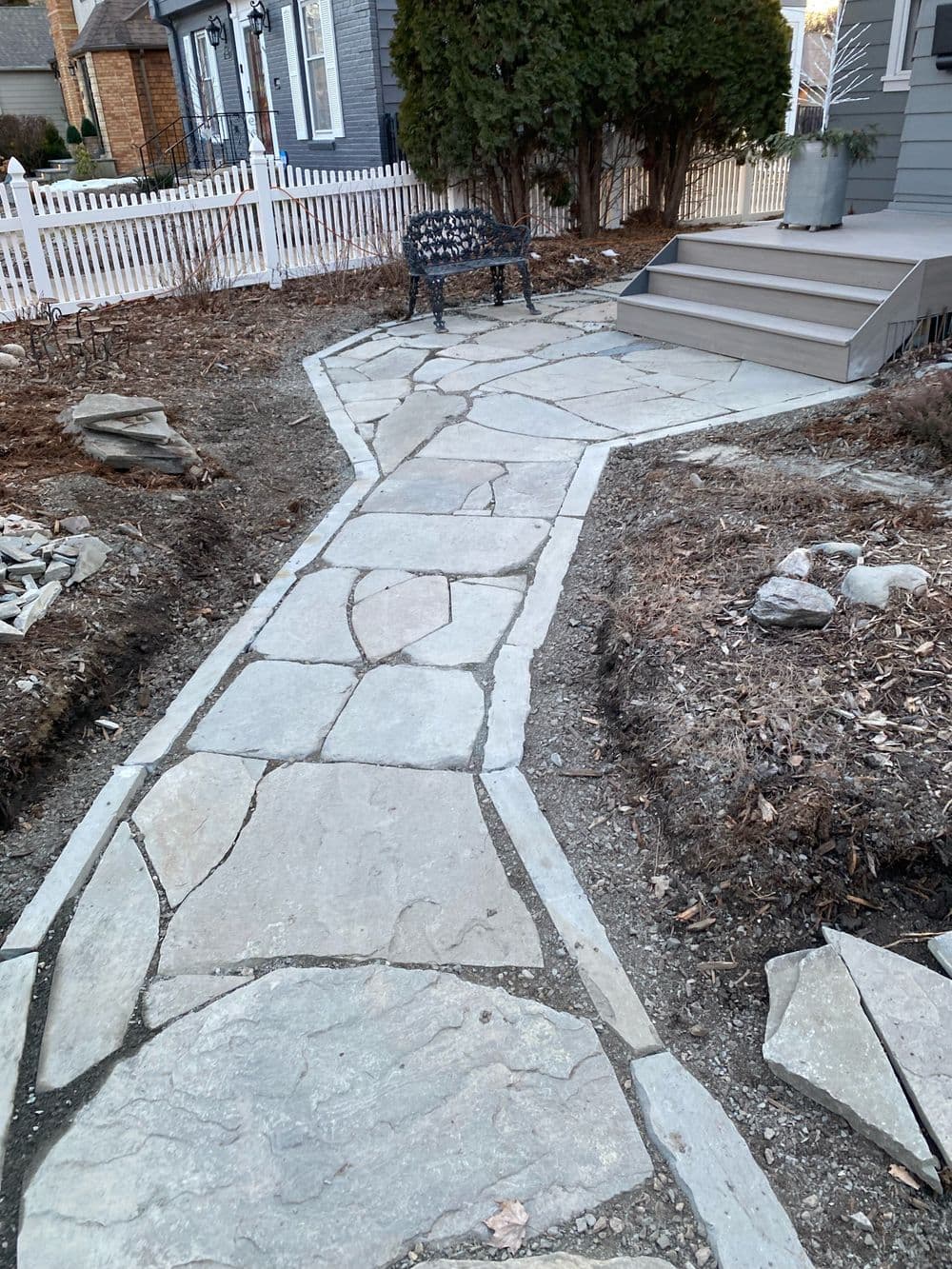 Stone pathway leading to a house with a bench and landscaped garden area.