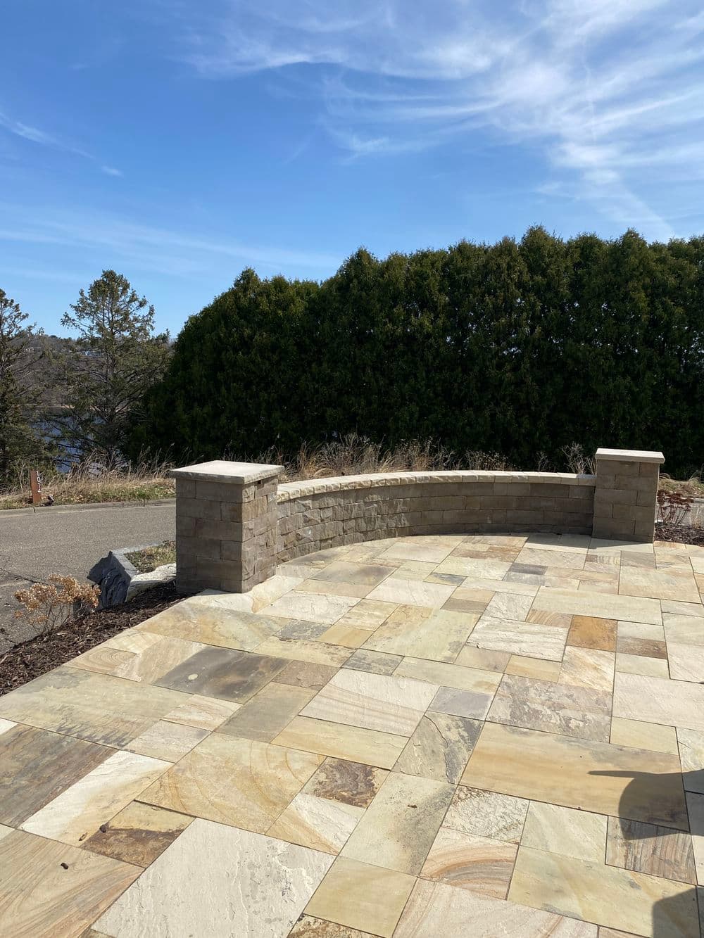 Curved stone patio with natural landscaping and blue sky in the background.