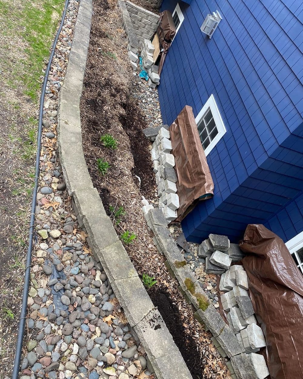 Blue house exterior with landscaped garden, stone path, and mulch along the foundation.