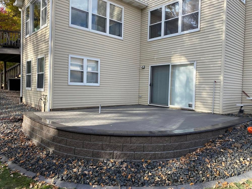 Modern patio with stone wall and sliding door, surrounded by gravel and house exterior.