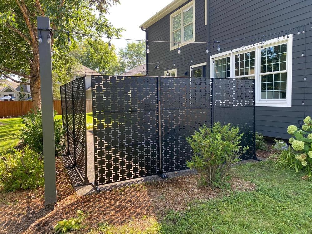 Modern black privacy screens in a landscaped yard by a gray house with string lights.