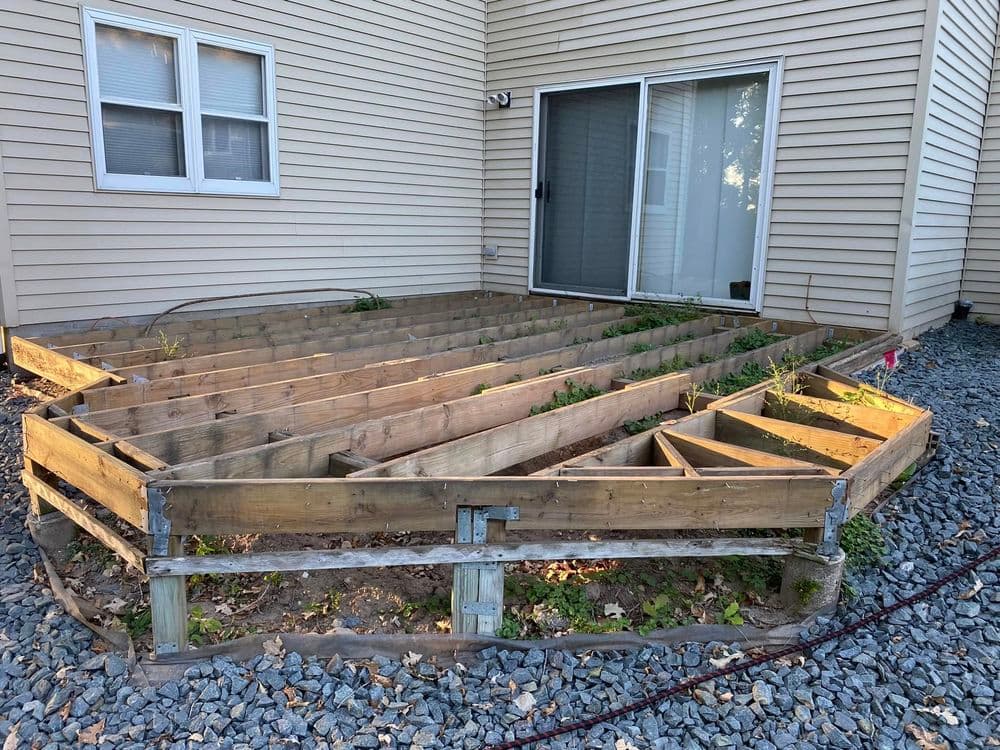 Raised garden bed frame with soil and plants near a house entrance.