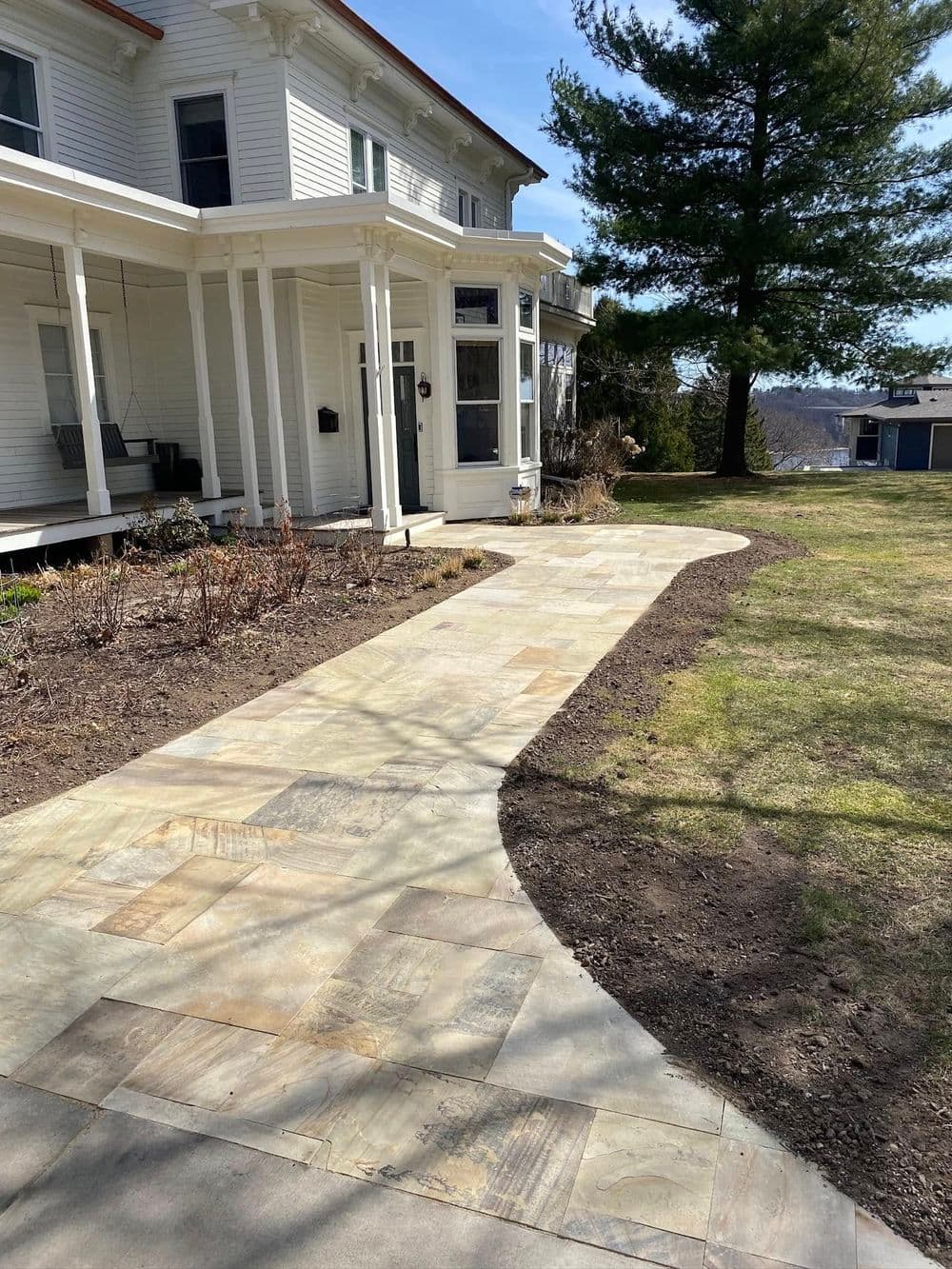 Pathway leading to a white house with a porch and landscaped yard under a blue sky.